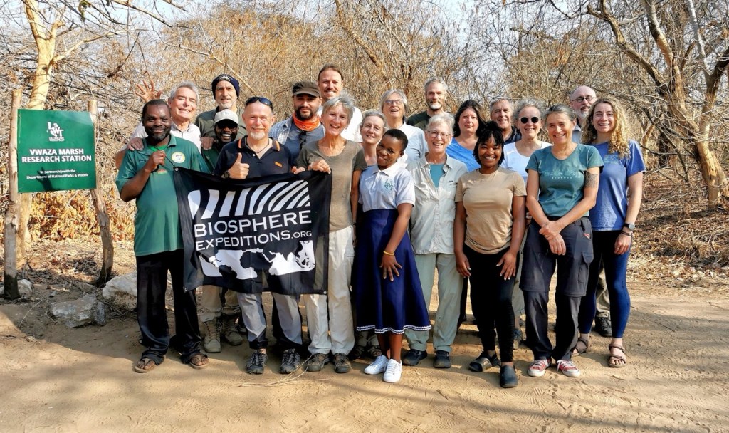 A group of people with a Biosphere Expeditions flag smiling into the camera