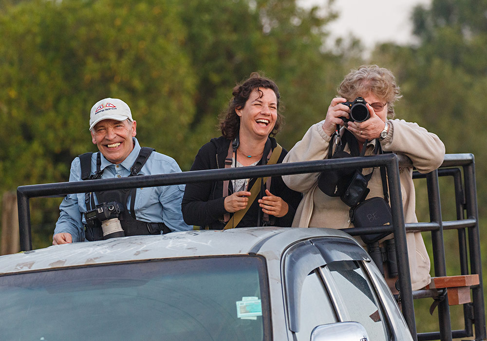 3 people standing in the back of a truck, one holiding a camera ready to take a picture