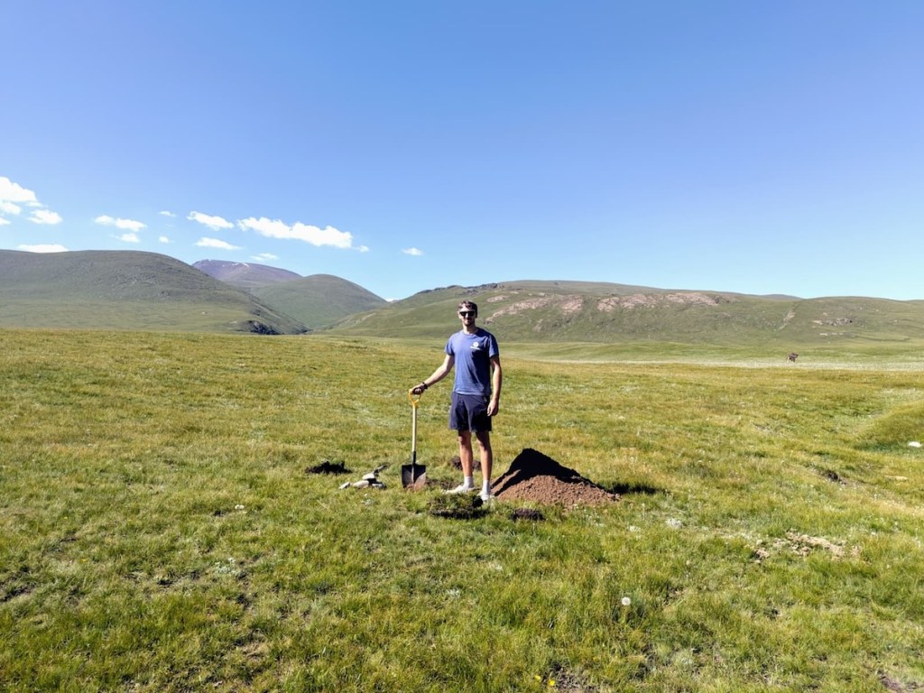 Man with a shovel next to a hole he has dug