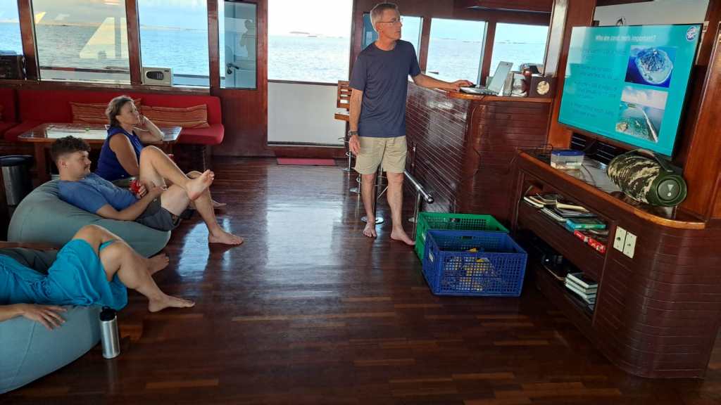 A teaching session - one person stands in front of a screen, the rest sit on bean bags, listening